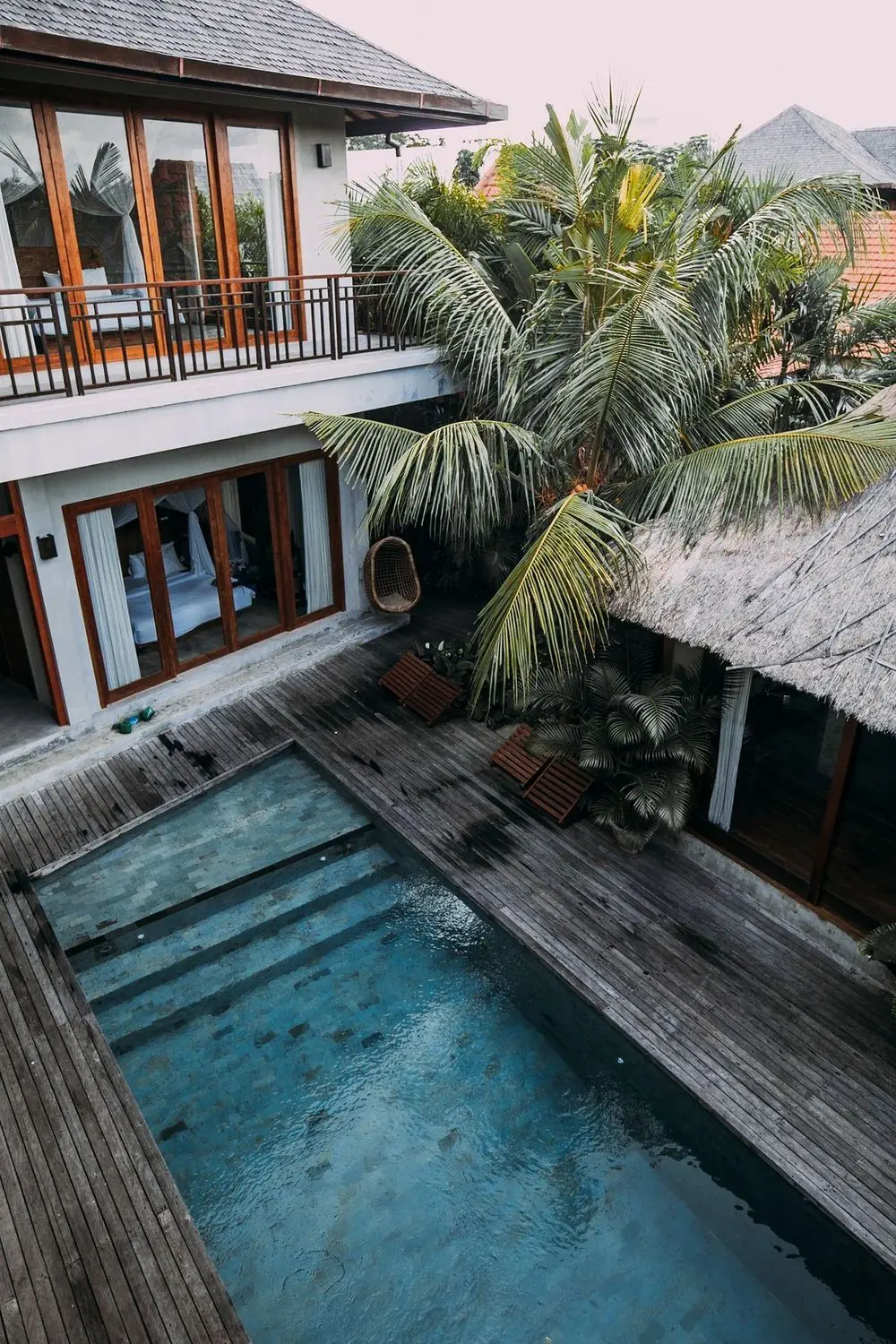 Wooden villa among tropical trees with a blue pool seen from above