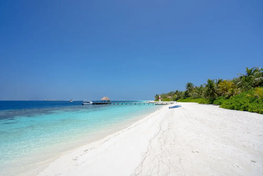 White sand beach with a jetty and thatched hut over turquoise shallows