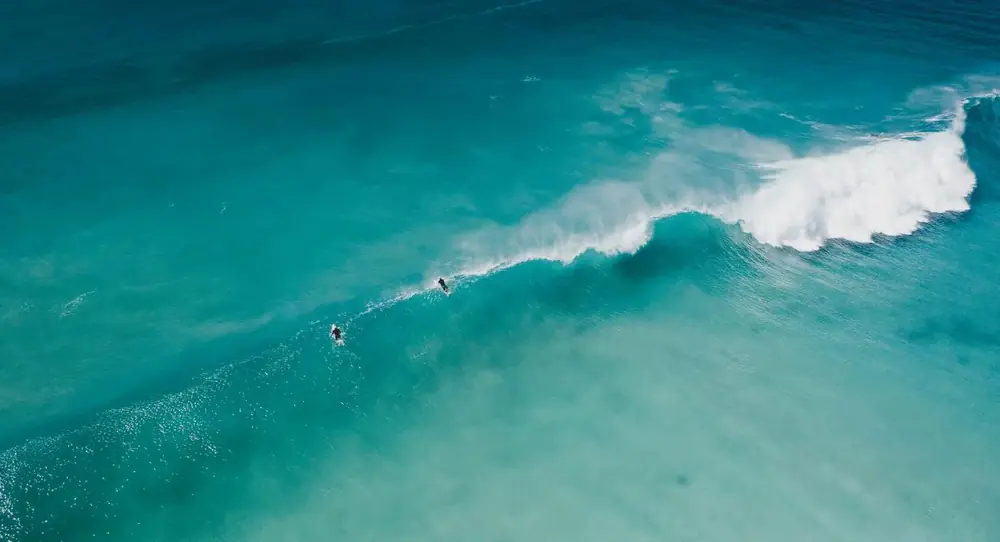 Turquoise sea seen from above, a single wave breaking over pale shallows